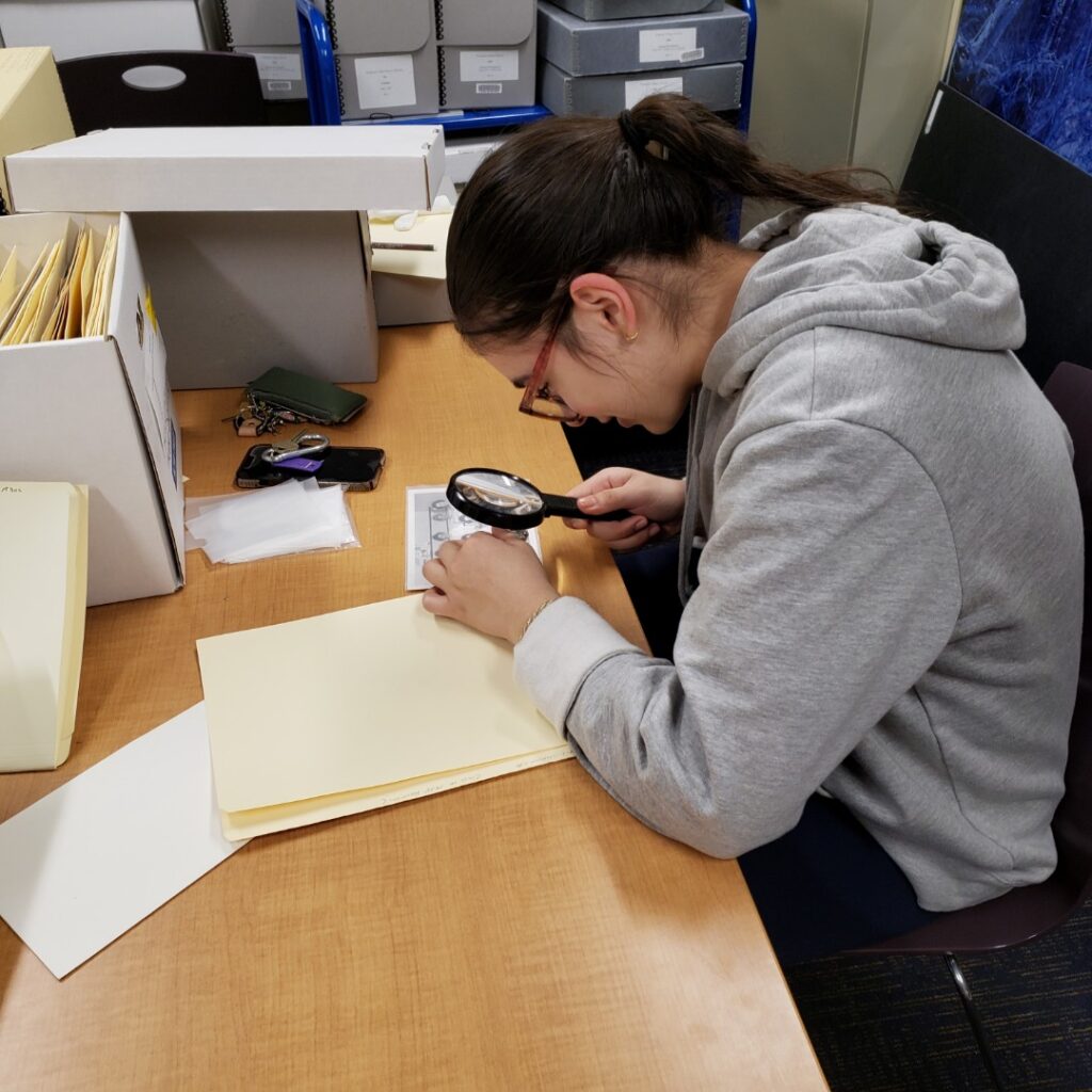 Photo of me using a magnifying glass to attempt to read the name tag on a woman's shirt.
